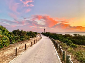 Road amidst trees against sky during sunset