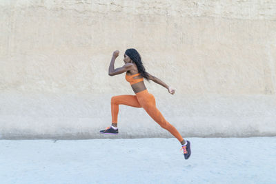 Side view of sportswoman jogging by wall