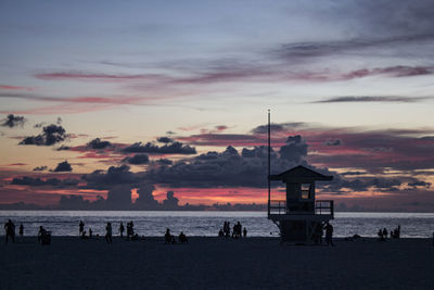 Silhouette people on beach against sky at sunset