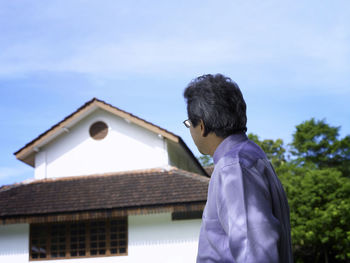 Man standing by house against sky