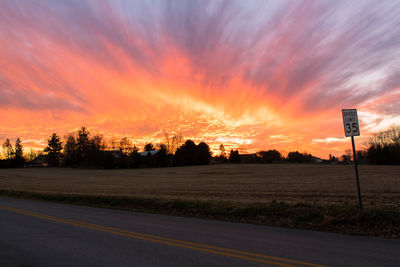 Road by trees against sky during sunset