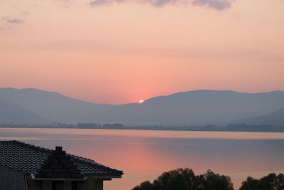 Silhouette buildings by lake and mountains against romantic sky at sunset