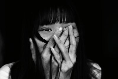 Close-up of happy young woman covering mouth while looking away against black background