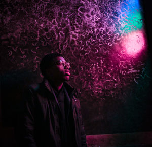 Young man looking away against illuminated light at night