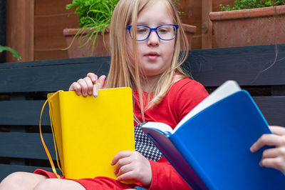 Two school age girls sitting together in garden and doing homework.