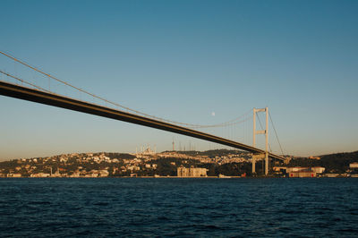 Suspension bridge over river in city against clear blue sky