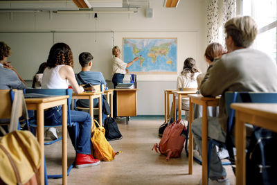 Female teacher teaching about map to girls and boys in classroom