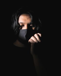 Close-up portrait of woman covering face against black background