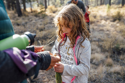 Girl in nature with family looking at pine needles in hand