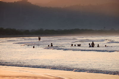 Silhouette people at beach against sky during sunset