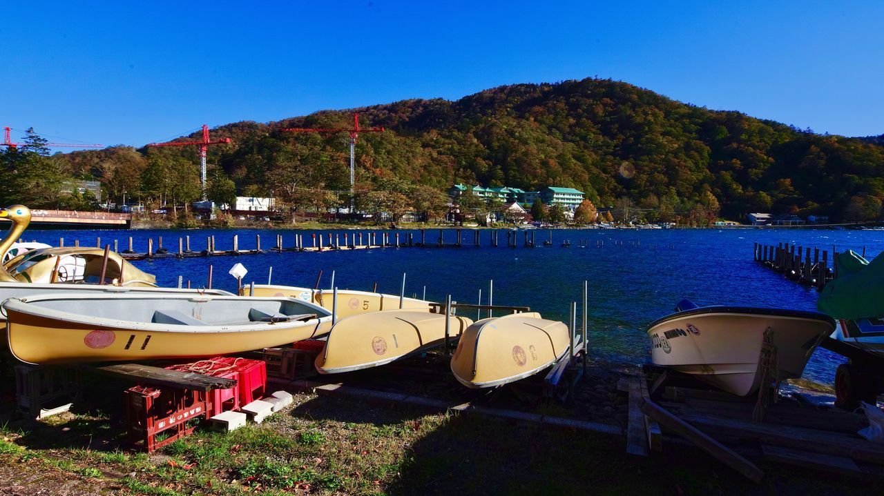 water, mountain, nautical vessel, transportation, moored, sky, nature, mode of transportation, no people, plant, lake, blue, tree, day, architecture, beauty in nature, sunlight, harbor, outdoors, yacht, sailboat, port