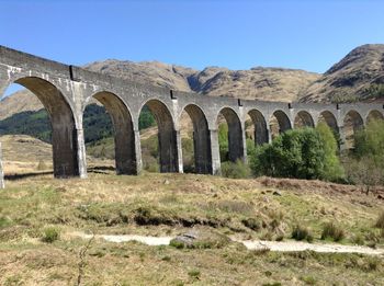 Arch bridge on field against clear sky