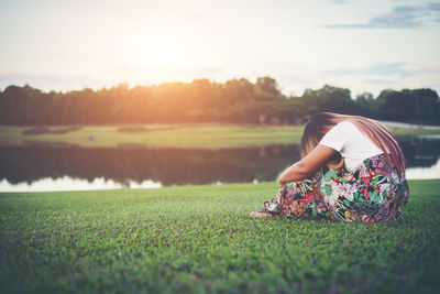 Depressed woman sitting on field during sunset