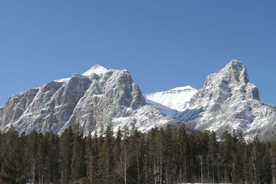 Low angle view of snowcapped mountains against clear blue sky