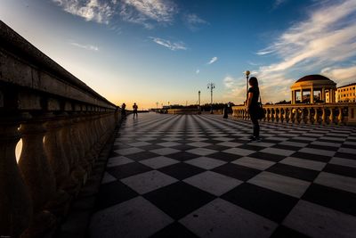 Woman standing on tiled floor against sky during sunset