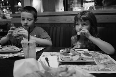 Siblings eating food at table in restaurant