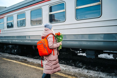 Girl on the platform of the station with a red backpack and a bouquet of tulip flowers