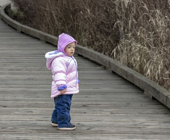 Cute baby girl wearing warm clothing standing on footpath