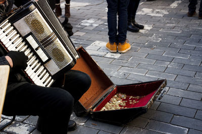 Low section of male street musician playing accordion on footpath