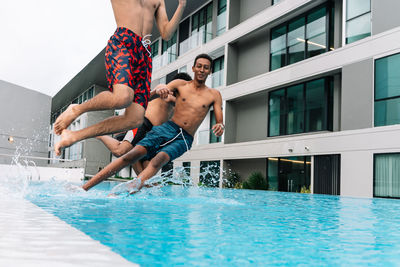 Three teenagers jumping into a pool surrounded by buildings