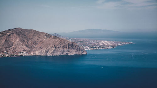Scenic view of blue sea and rocky mountains against sky on sunny day