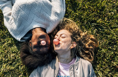 Two best friends making a gum bubble lying in the grass