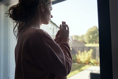 Side view of woman looking through window