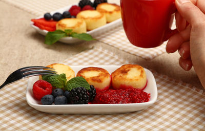 Cropped hand of woman holding cup by cheesecakes with berries and preserves on table