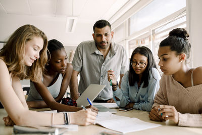 Female teenagers studying while professor standing by table in classroom