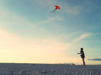 Woman flying kite at beach against sky