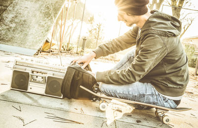 Side view of young man sitting on skateboard at park during sunset