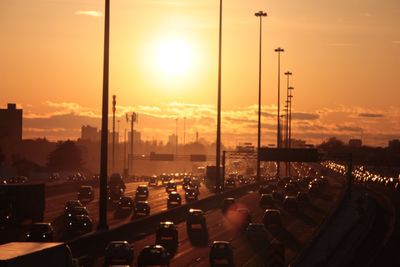 Cars on illuminated city against sky during sunset