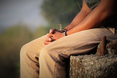 Midsection of man sitting on damaged retaining wall