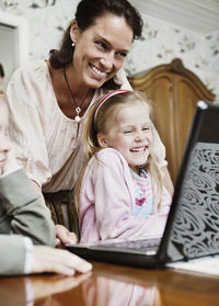 Happy mother and children looking at laptop in house