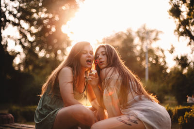 Girlfriends blowing bubbles while sitting in park during summer