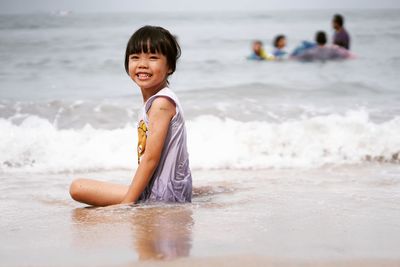 Portrait of smiling cute girl sitting on shore at beach