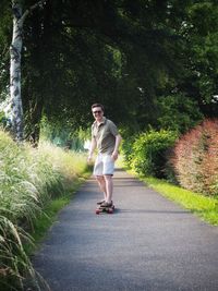 Portrait of smiling young woman skateboarding on road against trees