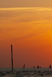 Silhouette people on beach against orange sky