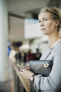 Businesswoman looking away while holding smart phone at airport