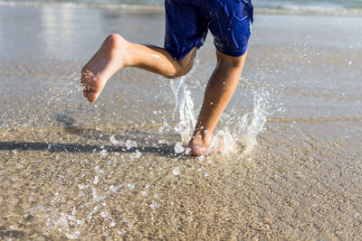 Low section of boy running on shore at beach