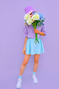 Full length of woman holding bouquet standing against colored background