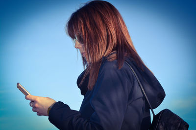 Woman using smart phone against clear blue sky