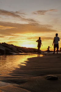 Silhouette people on beach against sky during sunset