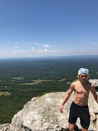 Shirtless man standing on rock against sky