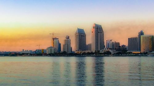 Sea by cityscape against sky during sunset