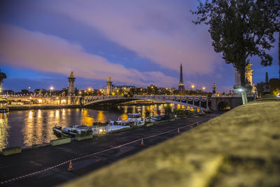 Illuminated bridge over river in city against sky at dusk