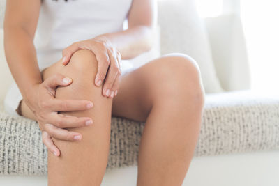 Midsection of woman suffering from knee pain while sitting at home