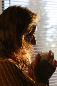 Woman holding a warm cup of coffee next to a window