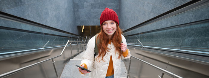 Portrait of young woman standing against escalator