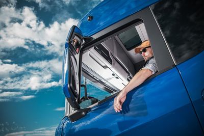 Reflection of man on car mirror against blue sky